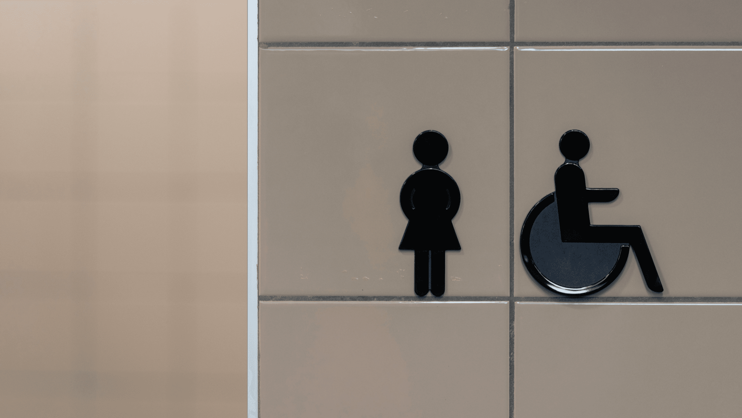 Black silhouette of female and wheelchair accessibility icons on a tan tiled wall.